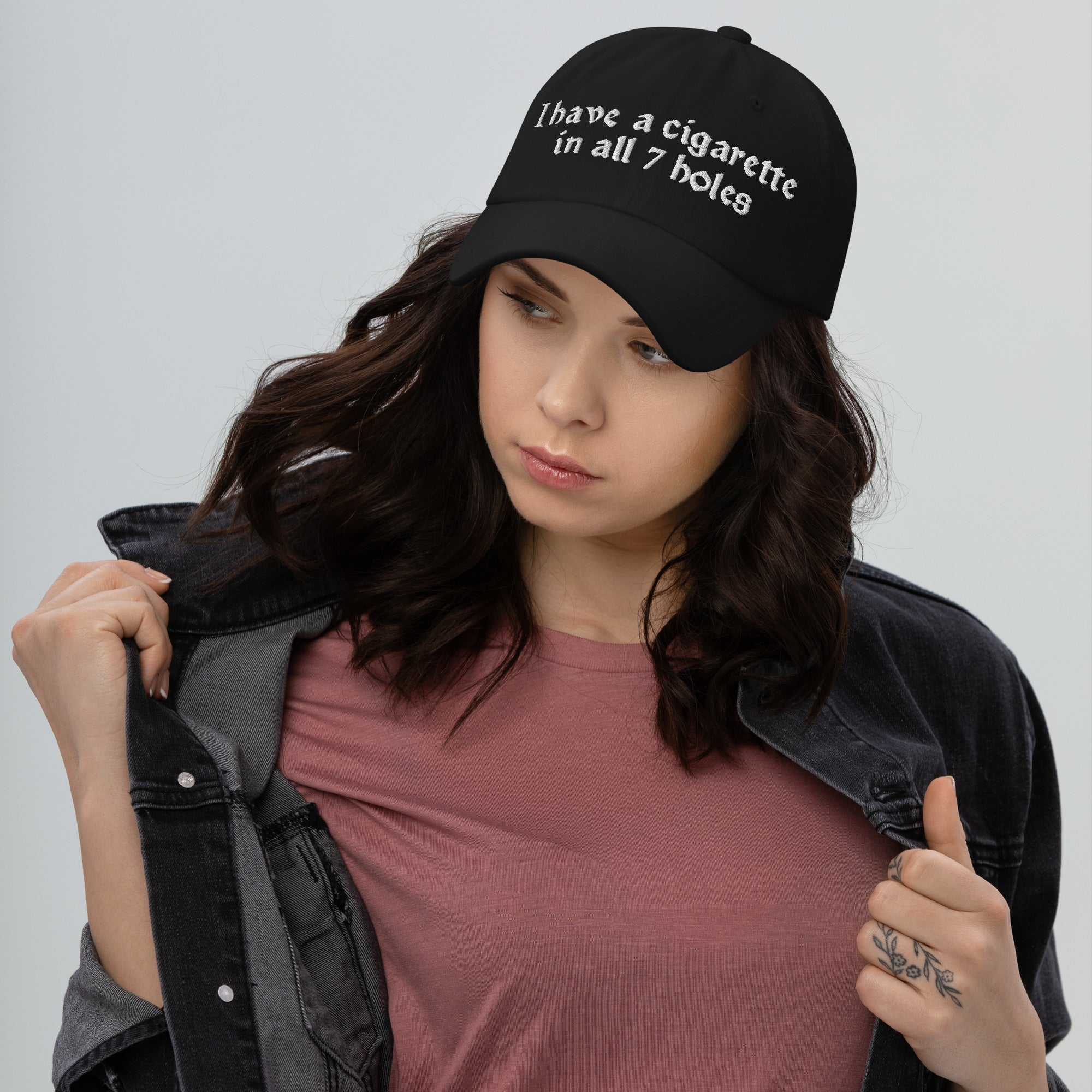 Baseball cap embroidered with the phrase ‘I Have a Cigarette in All 7 Holes’ in ornate vintage gothic lettering. Alternative fashion accessory with edgy internet humor, queer streetwear aesthetic, punk inspired style, ironic meme fashion, tattoo inspired typography, goth streetwear, adjustable dad hat, casual alternative outfit accessory, artsy statement cap, chaotic humor apparel, indie fashion, and expressive alternative clothing for concerts, festivals, everyday wear, and alternative wardrobes.