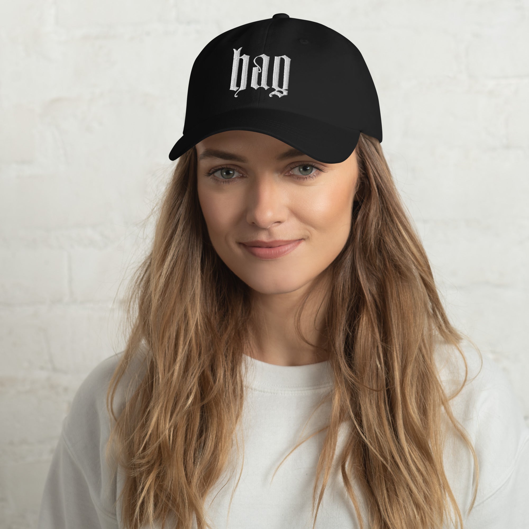 Black dad hat embroidered with the word ‘HAG’ in ornate vintage gothic lettering. Alternative fashion accessory with queer streetwear aesthetic, witchy fashion, sarcastic humor, feminist style, indie fashion, spooky cute apparel, gothic embroidery, punk inspired streetwear, adjustable baseball cap, casual everyday alternative outfit, internet humor fashion, artsy accessory, and edgy statement hat for concerts, festivals, casual wear, and alternative wardrobes.