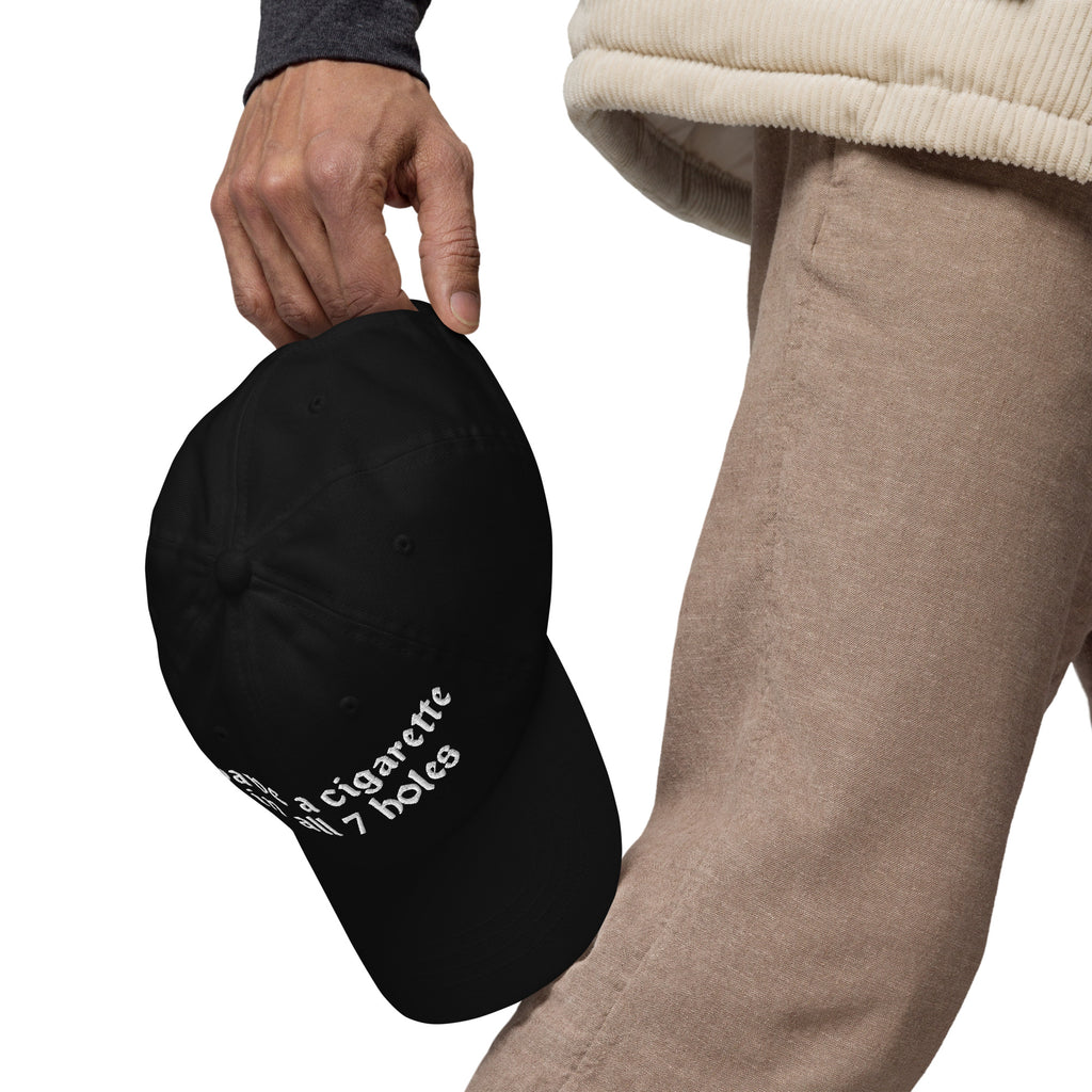 Baseball cap embroidered with the phrase ‘I Have a Cigarette in All 7 Holes’ in ornate vintage gothic lettering. Alternative fashion accessory with edgy internet humor, queer streetwear aesthetic, punk inspired style, ironic meme fashion, tattoo inspired typography, goth streetwear, adjustable dad hat, casual alternative outfit accessory, artsy statement cap, chaotic humor apparel, indie fashion, and expressive alternative clothing for concerts, festivals, everyday wear, and alternative wardrobes.