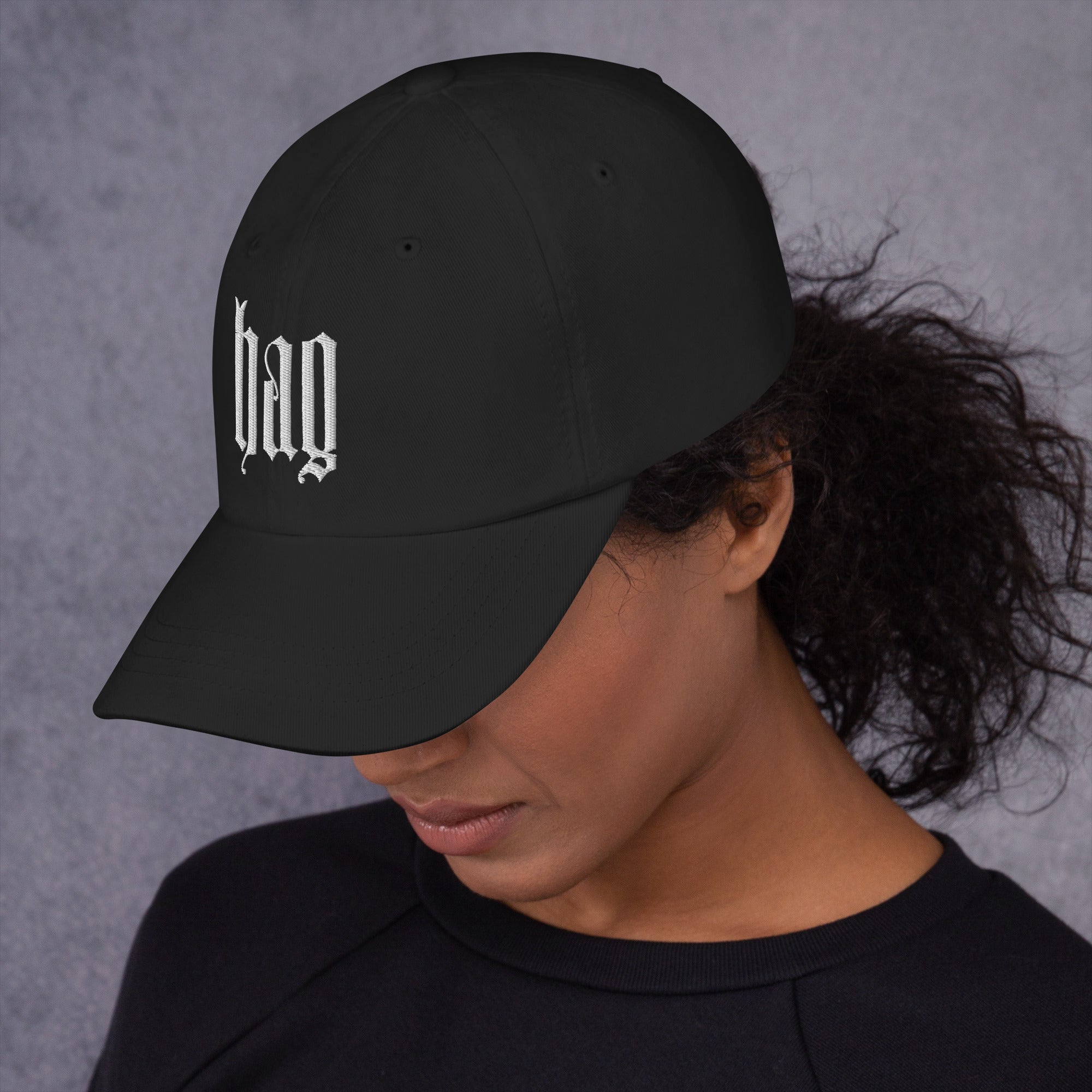 Black dad hat embroidered with the word ‘HAG’ in ornate vintage gothic lettering. Alternative fashion accessory with queer streetwear aesthetic, witchy fashion, sarcastic humor, feminist style, indie fashion, spooky cute apparel, gothic embroidery, punk inspired streetwear, adjustable baseball cap, casual everyday alternative outfit, internet humor fashion, artsy accessory, and edgy statement hat for concerts, festivals, casual wear, and alternative wardrobes.