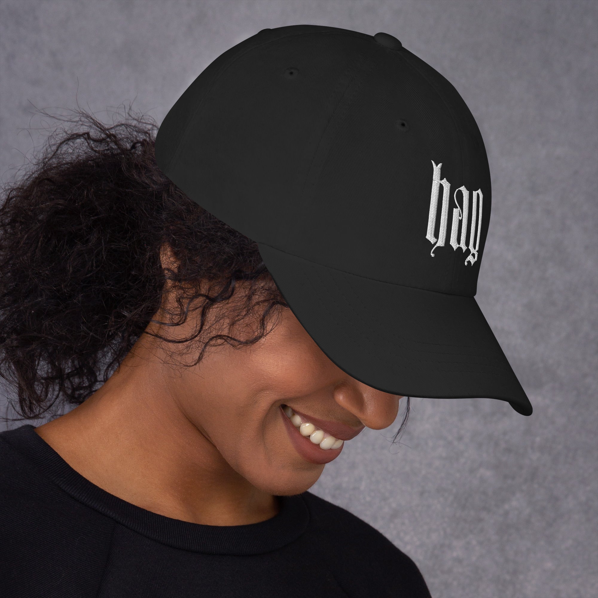 Black dad hat embroidered with the word ‘HAG’ in ornate vintage gothic lettering. Alternative fashion accessory with queer streetwear aesthetic, witchy fashion, sarcastic humor, feminist style, indie fashion, spooky cute apparel, gothic embroidery, punk inspired streetwear, adjustable baseball cap, casual everyday alternative outfit, internet humor fashion, artsy accessory, and edgy statement hat for concerts, festivals, casual wear, and alternative wardrobes.