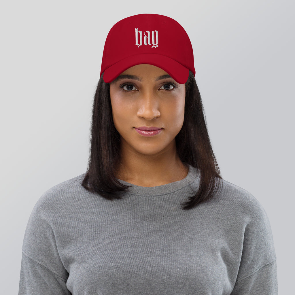 Black dad hat embroidered with the word ‘HAG’ in ornate vintage gothic lettering. Alternative fashion accessory with queer streetwear aesthetic, witchy fashion, sarcastic humor, feminist style, indie fashion, spooky cute apparel, gothic embroidery, punk inspired streetwear, adjustable baseball cap, casual everyday alternative outfit, internet humor fashion, artsy accessory, and edgy statement hat for concerts, festivals, casual wear, and alternative wardrobes.
