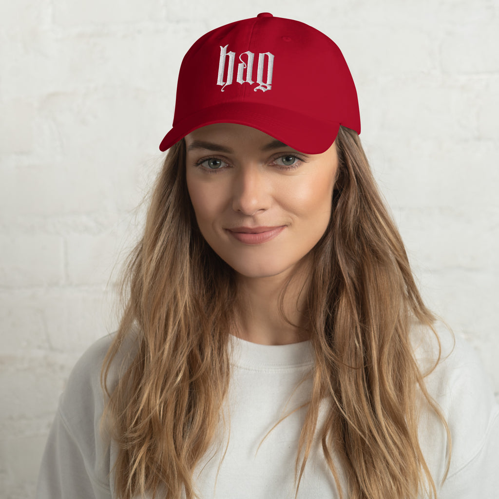 Black dad hat embroidered with the word ‘HAG’ in ornate vintage gothic lettering. Alternative fashion accessory with queer streetwear aesthetic, witchy fashion, sarcastic humor, feminist style, indie fashion, spooky cute apparel, gothic embroidery, punk inspired streetwear, adjustable baseball cap, casual everyday alternative outfit, internet humor fashion, artsy accessory, and edgy statement hat for concerts, festivals, casual wear, and alternative wardrobes.