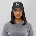 Black dad hat embroidered with the word ‘HAG’ in ornate vintage gothic lettering. Alternative fashion accessory with queer streetwear aesthetic, witchy fashion, sarcastic humor, feminist style, indie fashion, spooky cute apparel, gothic embroidery, punk inspired streetwear, adjustable baseball cap, casual everyday alternative outfit, internet humor fashion, artsy accessory, and edgy statement hat for concerts, festivals, casual wear, and alternative wardrobes.