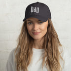 Black dad hat embroidered with the word ‘HAG’ in ornate vintage gothic lettering. Alternative fashion accessory with queer streetwear aesthetic, witchy fashion, sarcastic humor, feminist style, indie fashion, spooky cute apparel, gothic embroidery, punk inspired streetwear, adjustable baseball cap, casual everyday alternative outfit, internet humor fashion, artsy accessory, and edgy statement hat for concerts, festivals, casual wear, and alternative wardrobes.