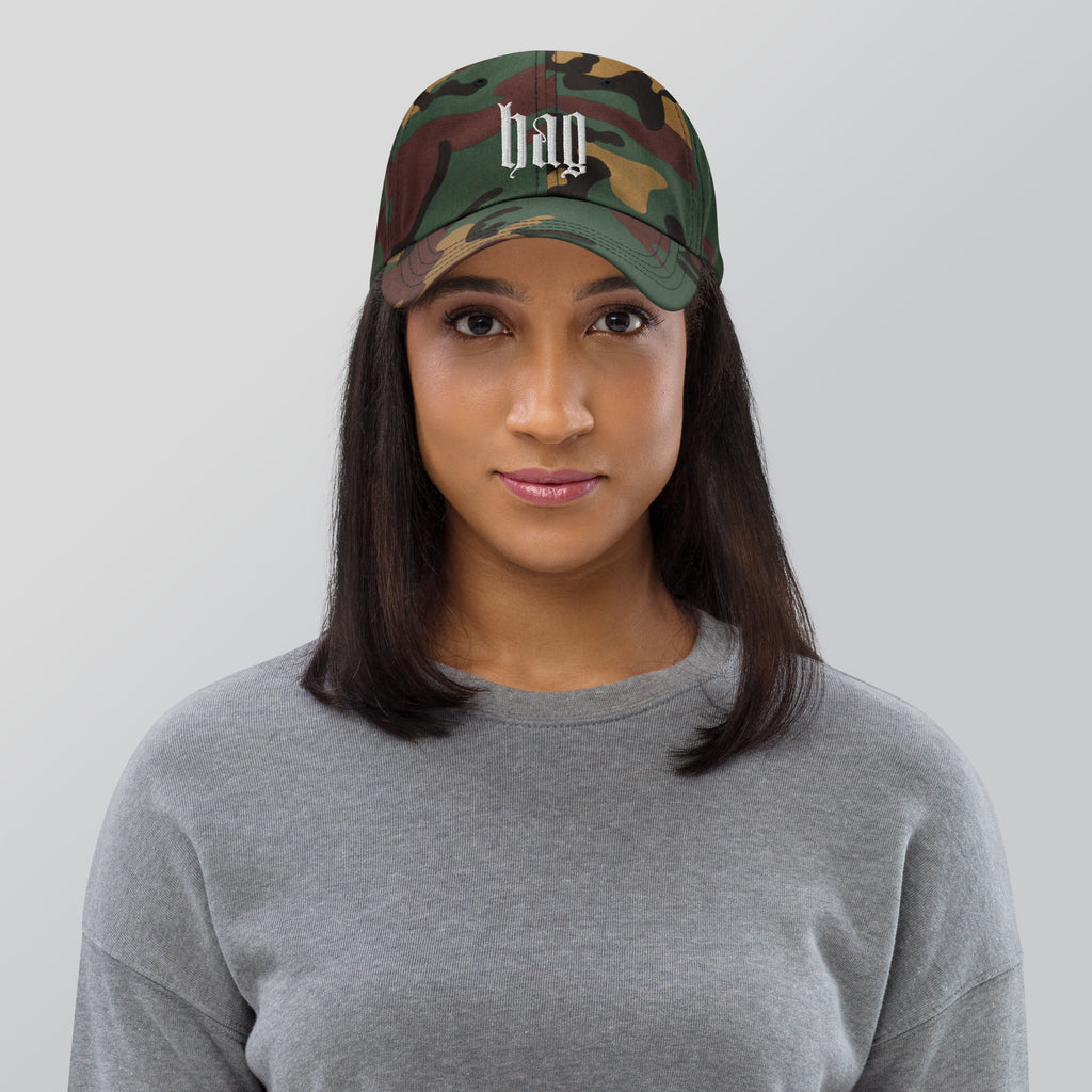 Black dad hat embroidered with the word ‘HAG’ in ornate vintage gothic lettering. Alternative fashion accessory with queer streetwear aesthetic, witchy fashion, sarcastic humor, feminist style, indie fashion, spooky cute apparel, gothic embroidery, punk inspired streetwear, adjustable baseball cap, casual everyday alternative outfit, internet humor fashion, artsy accessory, and edgy statement hat for concerts, festivals, casual wear, and alternative wardrobes.
