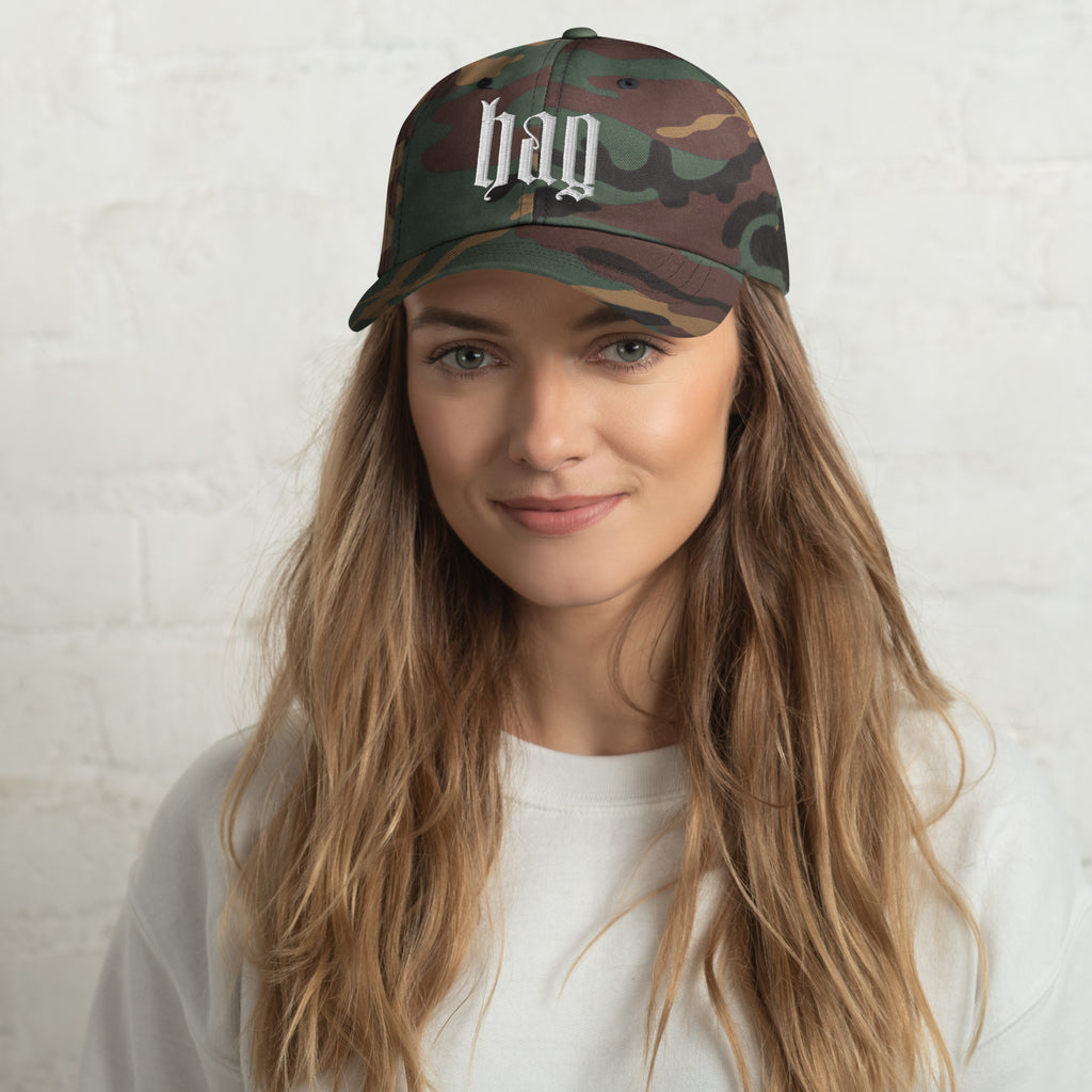 Black dad hat embroidered with the word ‘HAG’ in ornate vintage gothic lettering. Alternative fashion accessory with queer streetwear aesthetic, witchy fashion, sarcastic humor, feminist style, indie fashion, spooky cute apparel, gothic embroidery, punk inspired streetwear, adjustable baseball cap, casual everyday alternative outfit, internet humor fashion, artsy accessory, and edgy statement hat for concerts, festivals, casual wear, and alternative wardrobes.