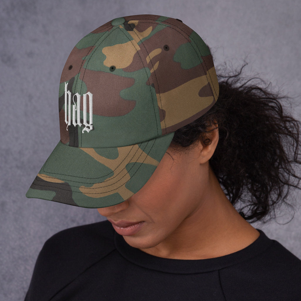 Black dad hat embroidered with the word ‘HAG’ in ornate vintage gothic lettering. Alternative fashion accessory with queer streetwear aesthetic, witchy fashion, sarcastic humor, feminist style, indie fashion, spooky cute apparel, gothic embroidery, punk inspired streetwear, adjustable baseball cap, casual everyday alternative outfit, internet humor fashion, artsy accessory, and edgy statement hat for concerts, festivals, casual wear, and alternative wardrobes.