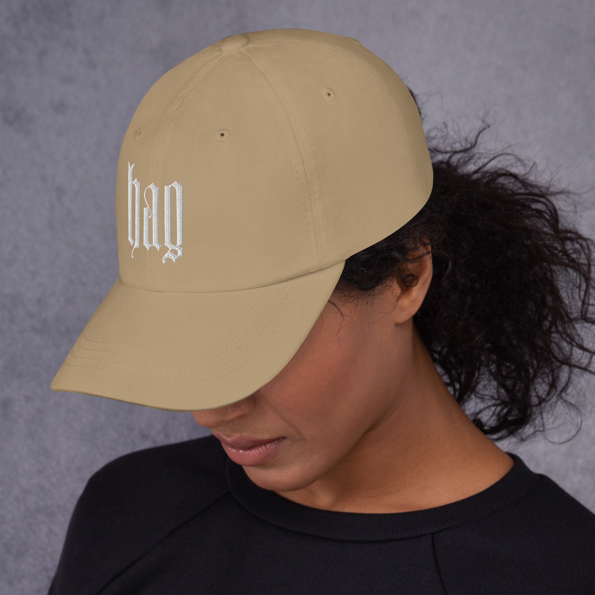 Black dad hat embroidered with the word ‘HAG’ in ornate vintage gothic lettering. Alternative fashion accessory with queer streetwear aesthetic, witchy fashion, sarcastic humor, feminist style, indie fashion, spooky cute apparel, gothic embroidery, punk inspired streetwear, adjustable baseball cap, casual everyday alternative outfit, internet humor fashion, artsy accessory, and edgy statement hat for concerts, festivals, casual wear, and alternative wardrobes.