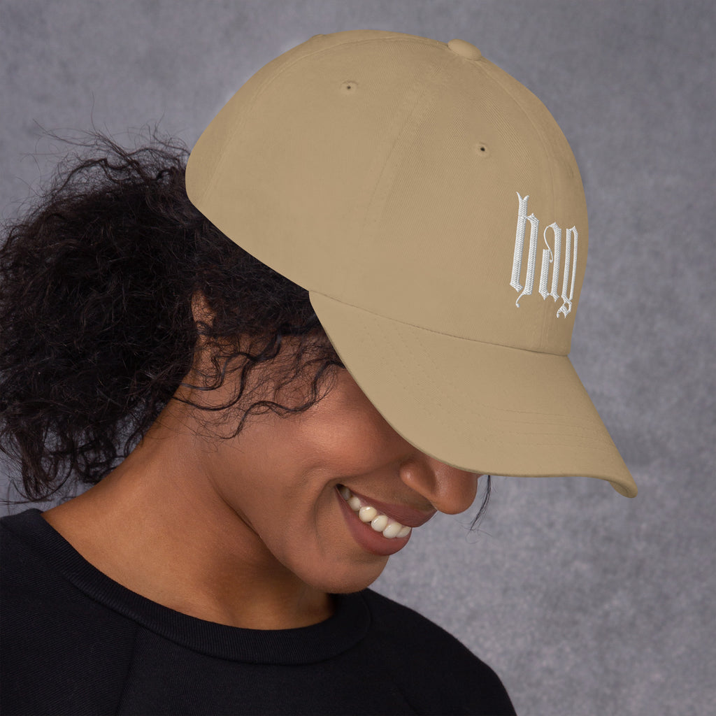 Black dad hat embroidered with the word ‘HAG’ in ornate vintage gothic lettering. Alternative fashion accessory with queer streetwear aesthetic, witchy fashion, sarcastic humor, feminist style, indie fashion, spooky cute apparel, gothic embroidery, punk inspired streetwear, adjustable baseball cap, casual everyday alternative outfit, internet humor fashion, artsy accessory, and edgy statement hat for concerts, festivals, casual wear, and alternative wardrobes.