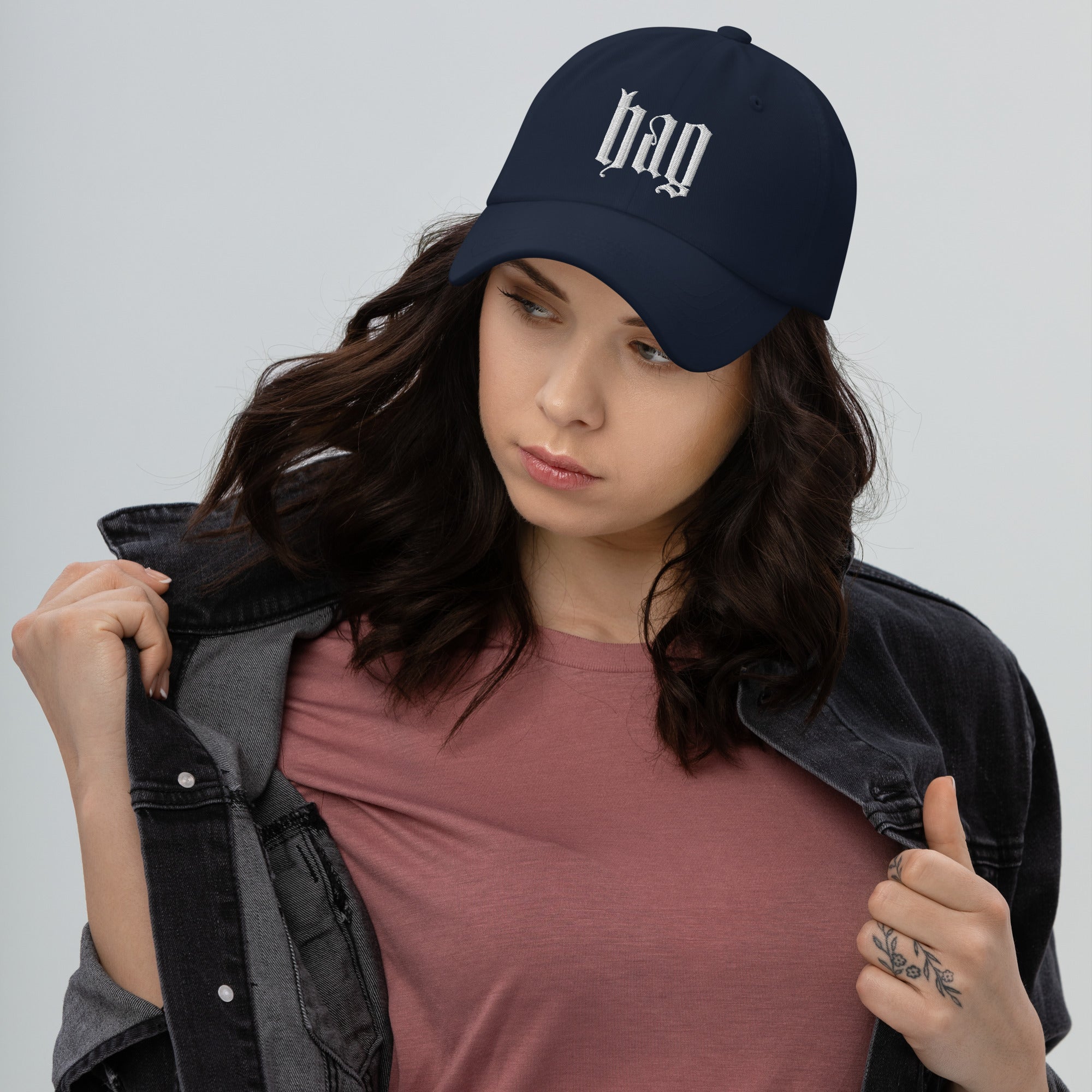 Black dad hat embroidered with the word ‘HAG’ in ornate vintage gothic lettering. Alternative fashion accessory with queer streetwear aesthetic, witchy fashion, sarcastic humor, feminist style, indie fashion, spooky cute apparel, gothic embroidery, punk inspired streetwear, adjustable baseball cap, casual everyday alternative outfit, internet humor fashion, artsy accessory, and edgy statement hat for concerts, festivals, casual wear, and alternative wardrobes.