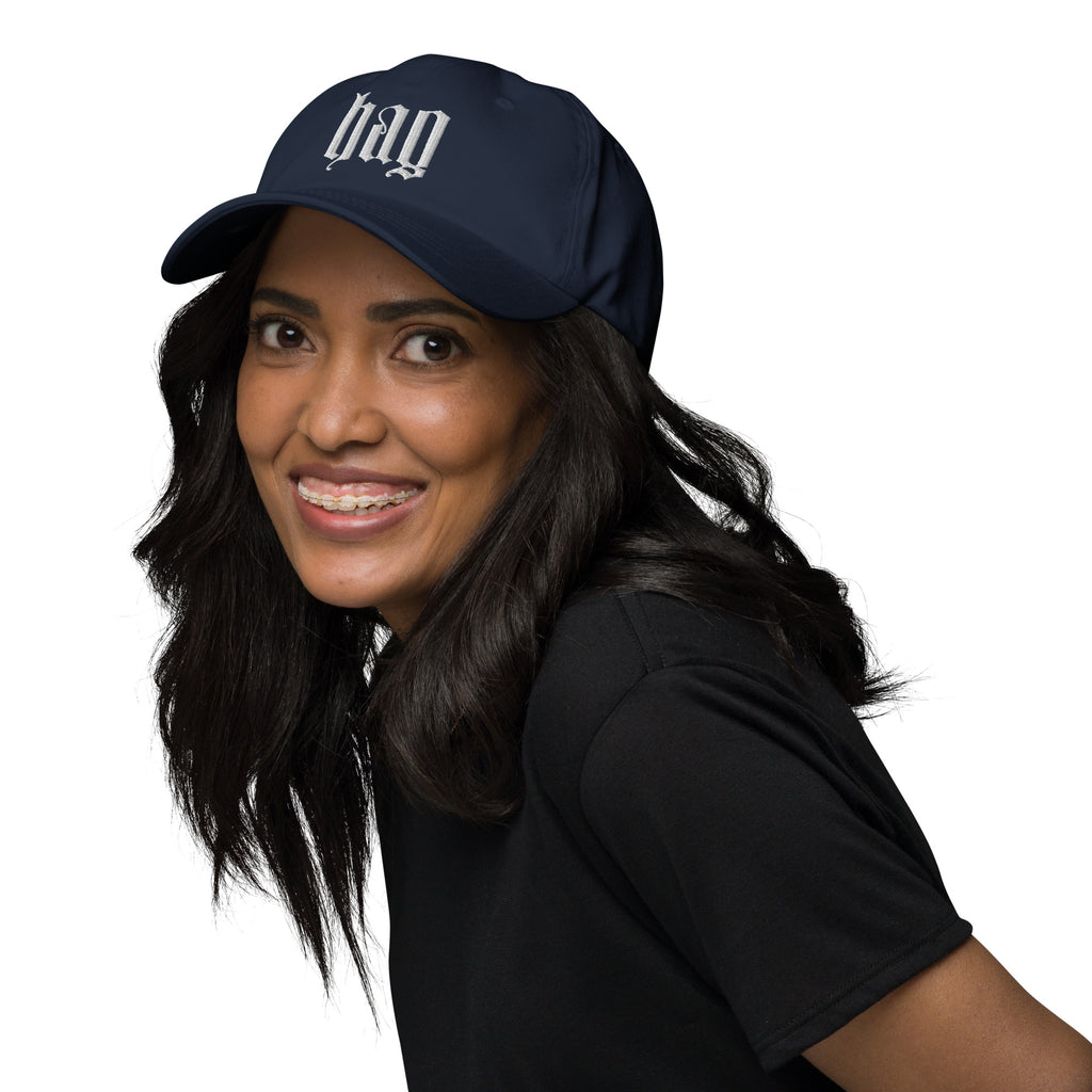 Black dad hat embroidered with the word ‘HAG’ in ornate vintage gothic lettering. Alternative fashion accessory with queer streetwear aesthetic, witchy fashion, sarcastic humor, feminist style, indie fashion, spooky cute apparel, gothic embroidery, punk inspired streetwear, adjustable baseball cap, casual everyday alternative outfit, internet humor fashion, artsy accessory, and edgy statement hat for concerts, festivals, casual wear, and alternative wardrobes.