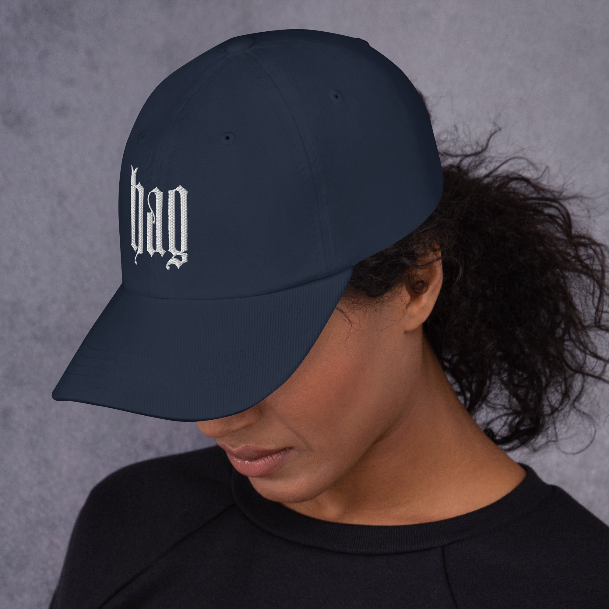Black dad hat embroidered with the word ‘HAG’ in ornate vintage gothic lettering. Alternative fashion accessory with queer streetwear aesthetic, witchy fashion, sarcastic humor, feminist style, indie fashion, spooky cute apparel, gothic embroidery, punk inspired streetwear, adjustable baseball cap, casual everyday alternative outfit, internet humor fashion, artsy accessory, and edgy statement hat for concerts, festivals, casual wear, and alternative wardrobes.