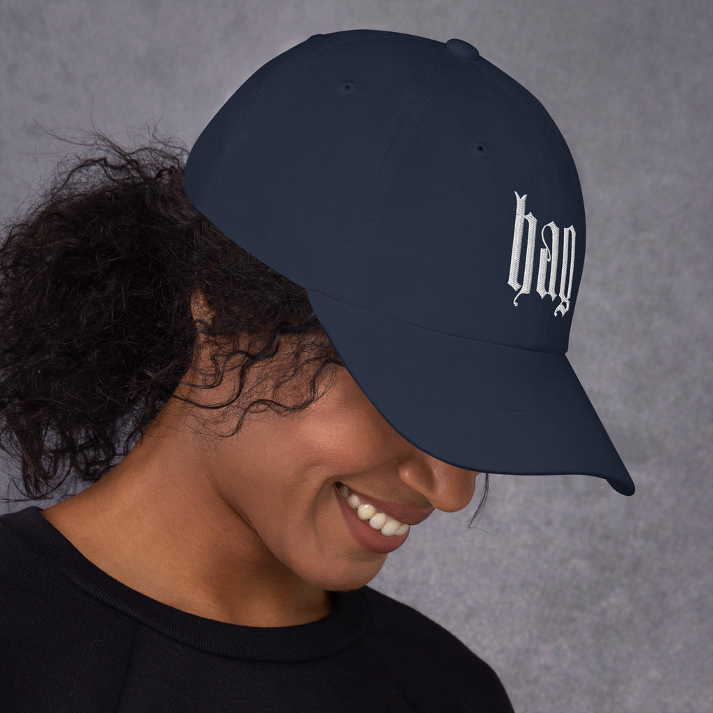Black dad hat embroidered with the word ‘HAG’ in ornate vintage gothic lettering. Alternative fashion accessory with queer streetwear aesthetic, witchy fashion, sarcastic humor, feminist style, indie fashion, spooky cute apparel, gothic embroidery, punk inspired streetwear, adjustable baseball cap, casual everyday alternative outfit, internet humor fashion, artsy accessory, and edgy statement hat for concerts, festivals, casual wear, and alternative wardrobes.