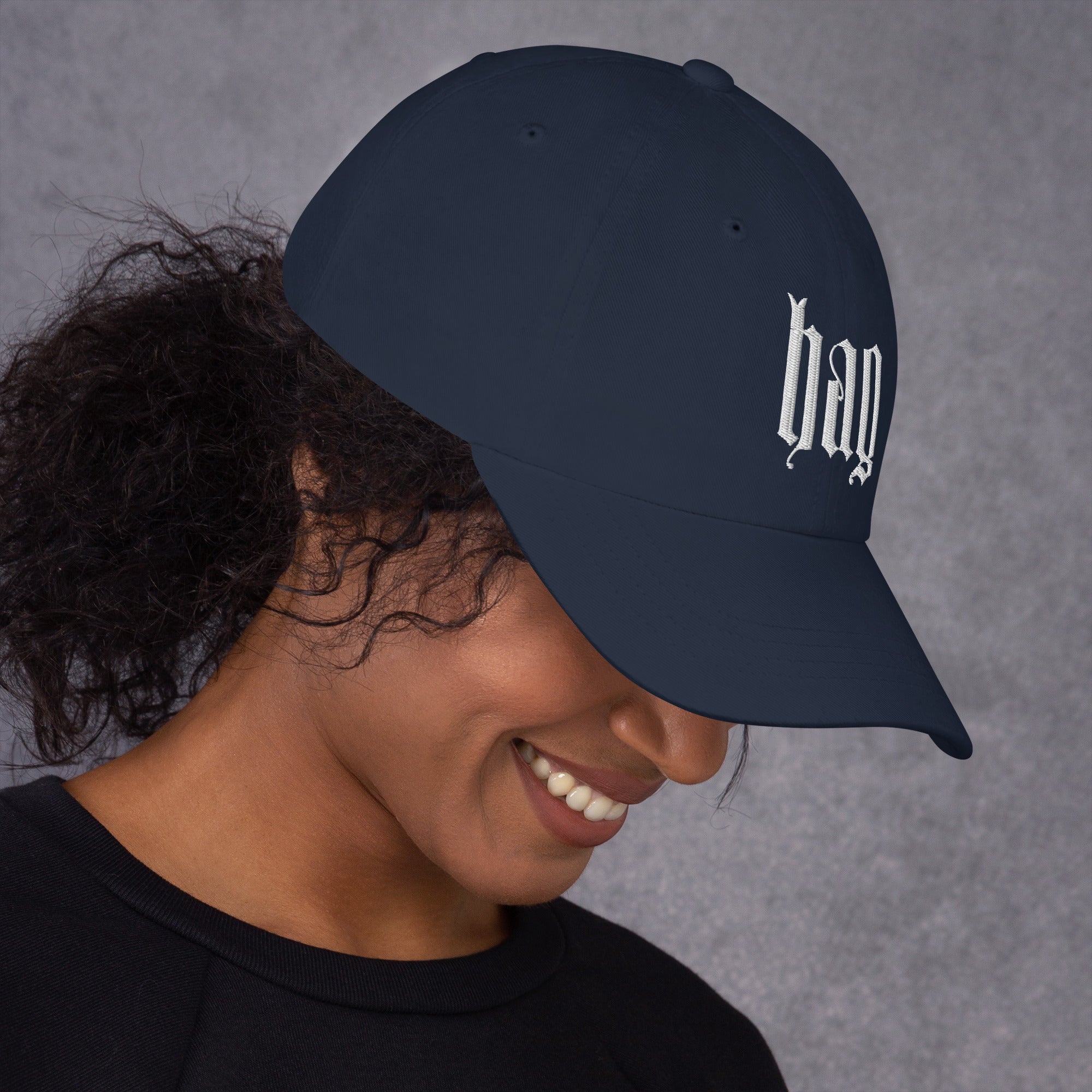 Black dad hat embroidered with the word ‘HAG’ in ornate vintage gothic lettering. Alternative fashion accessory with queer streetwear aesthetic, witchy fashion, sarcastic humor, feminist style, indie fashion, spooky cute apparel, gothic embroidery, punk inspired streetwear, adjustable baseball cap, casual everyday alternative outfit, internet humor fashion, artsy accessory, and edgy statement hat for concerts, festivals, casual wear, and alternative wardrobes.