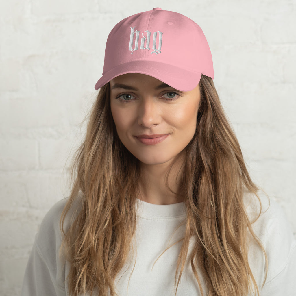 Black dad hat embroidered with the word ‘HAG’ in ornate vintage gothic lettering. Alternative fashion accessory with queer streetwear aesthetic, witchy fashion, sarcastic humor, feminist style, indie fashion, spooky cute apparel, gothic embroidery, punk inspired streetwear, adjustable baseball cap, casual everyday alternative outfit, internet humor fashion, artsy accessory, and edgy statement hat for concerts, festivals, casual wear, and alternative wardrobes.