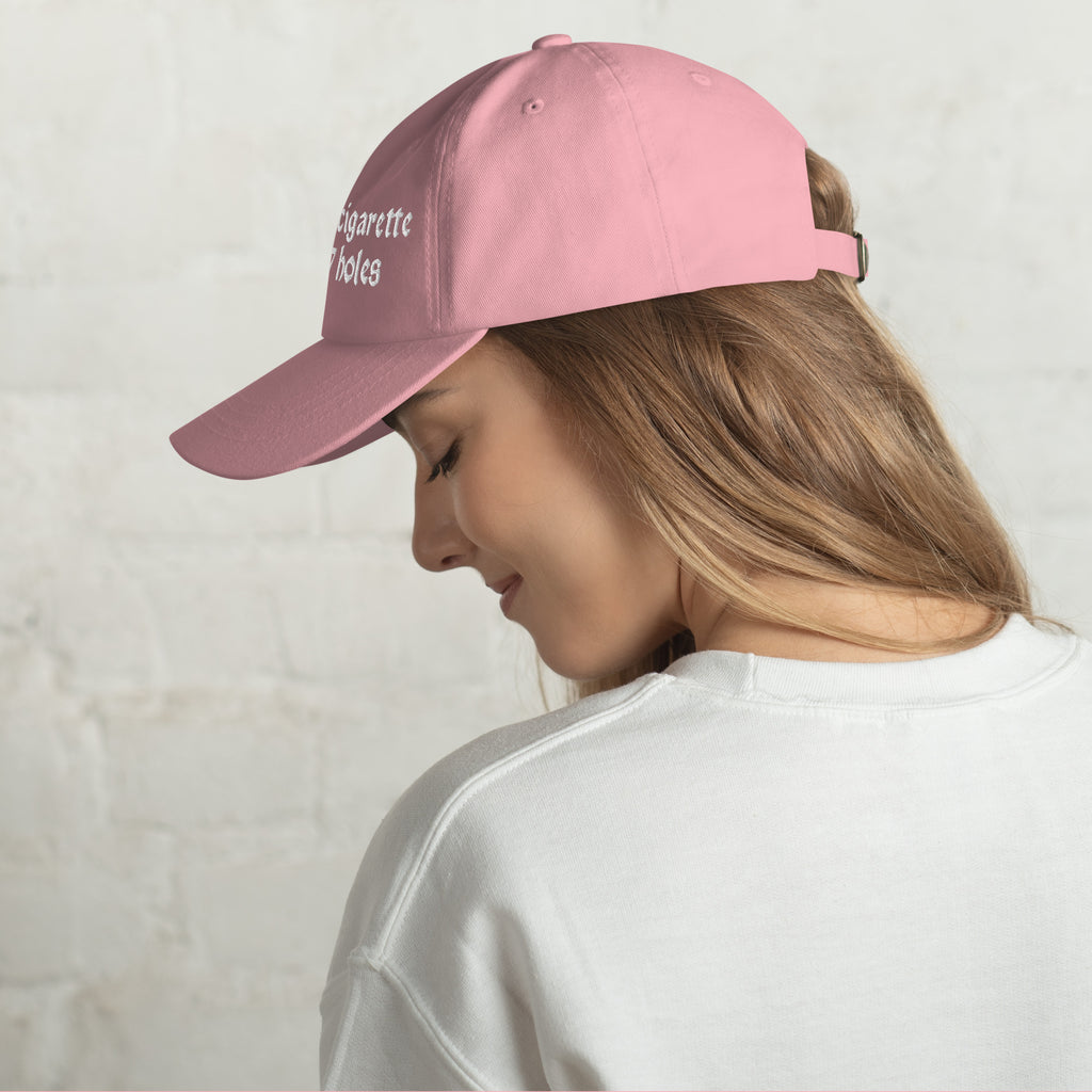 Baseball cap embroidered with the phrase ‘I Have a Cigarette in All 7 Holes’ in ornate vintage gothic lettering. Alternative fashion accessory with edgy internet humor, queer streetwear aesthetic, punk inspired style, ironic meme fashion, tattoo inspired typography, goth streetwear, adjustable dad hat, casual alternative outfit accessory, artsy statement cap, chaotic humor apparel, indie fashion, and expressive alternative clothing for concerts, festivals, everyday wear, and alternative wardrobes.