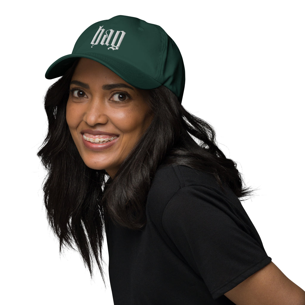 Black dad hat embroidered with the word ‘HAG’ in ornate vintage gothic lettering. Alternative fashion accessory with queer streetwear aesthetic, witchy fashion, sarcastic humor, feminist style, indie fashion, spooky cute apparel, gothic embroidery, punk inspired streetwear, adjustable baseball cap, casual everyday alternative outfit, internet humor fashion, artsy accessory, and edgy statement hat for concerts, festivals, casual wear, and alternative wardrobes.