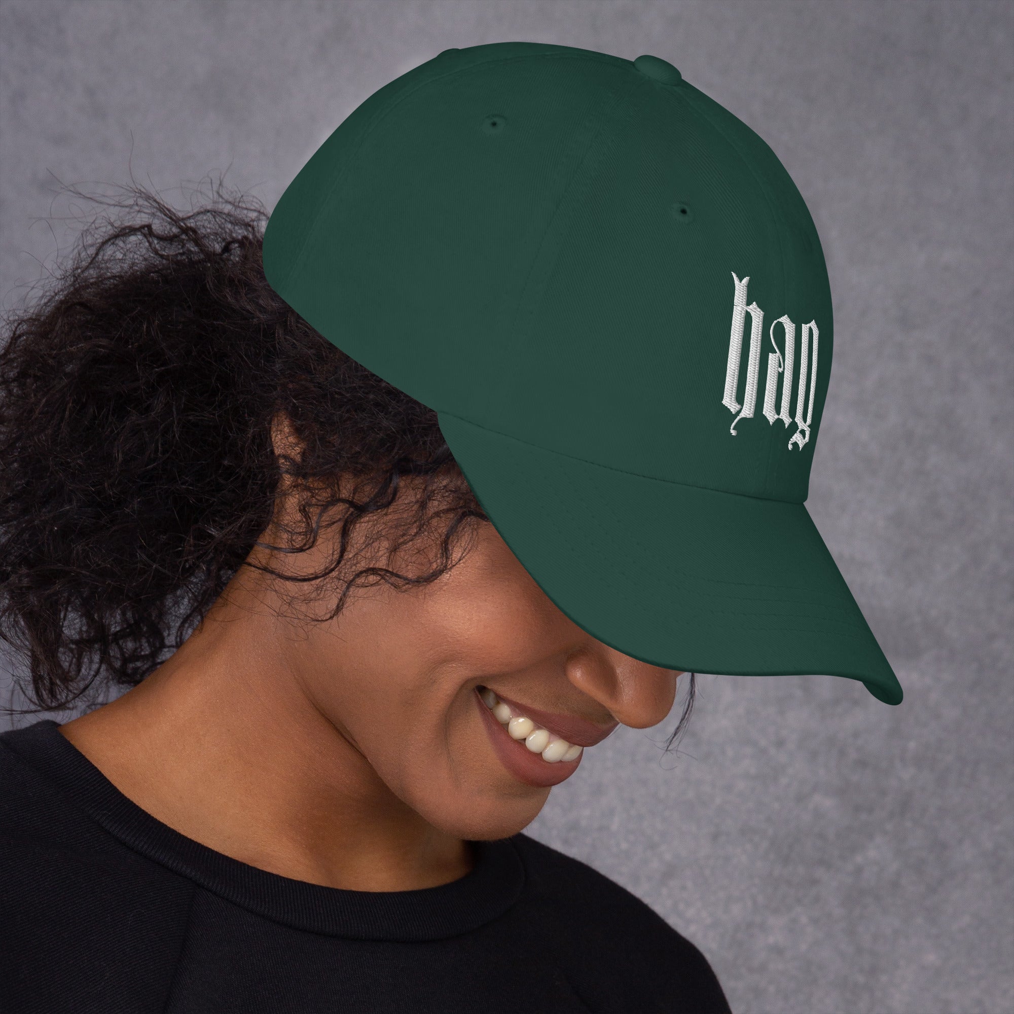 Black dad hat embroidered with the word ‘HAG’ in ornate vintage gothic lettering. Alternative fashion accessory with queer streetwear aesthetic, witchy fashion, sarcastic humor, feminist style, indie fashion, spooky cute apparel, gothic embroidery, punk inspired streetwear, adjustable baseball cap, casual everyday alternative outfit, internet humor fashion, artsy accessory, and edgy statement hat for concerts, festivals, casual wear, and alternative wardrobes.