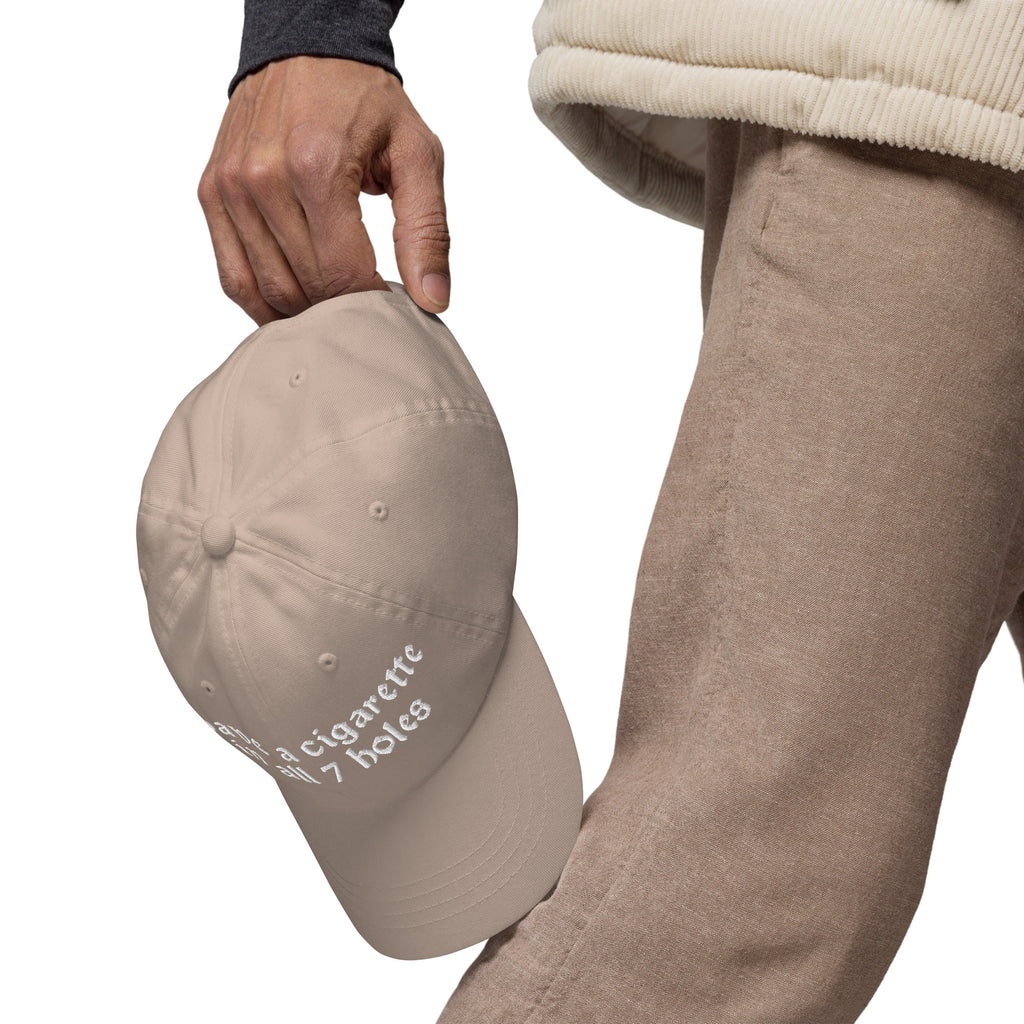 Baseball cap embroidered with the phrase ‘I Have a Cigarette in All 7 Holes’ in ornate vintage gothic lettering. Alternative fashion accessory with edgy internet humor, queer streetwear aesthetic, punk inspired style, ironic meme fashion, tattoo inspired typography, goth streetwear, adjustable dad hat, casual alternative outfit accessory, artsy statement cap, chaotic humor apparel, indie fashion, and expressive alternative clothing for concerts, festivals, everyday wear, and alternative wardrobes.