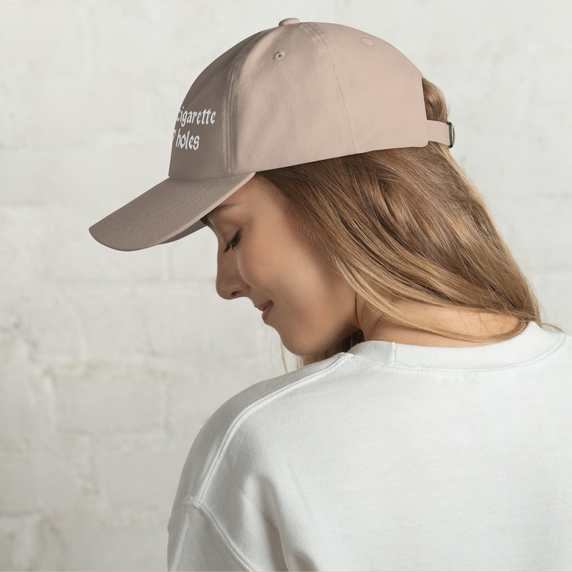 Baseball cap embroidered with the phrase ‘I Have a Cigarette in All 7 Holes’ in ornate vintage gothic lettering. Alternative fashion accessory with edgy internet humor, queer streetwear aesthetic, punk inspired style, ironic meme fashion, tattoo inspired typography, goth streetwear, adjustable dad hat, casual alternative outfit accessory, artsy statement cap, chaotic humor apparel, indie fashion, and expressive alternative clothing for concerts, festivals, everyday wear, and alternative wardrobes.